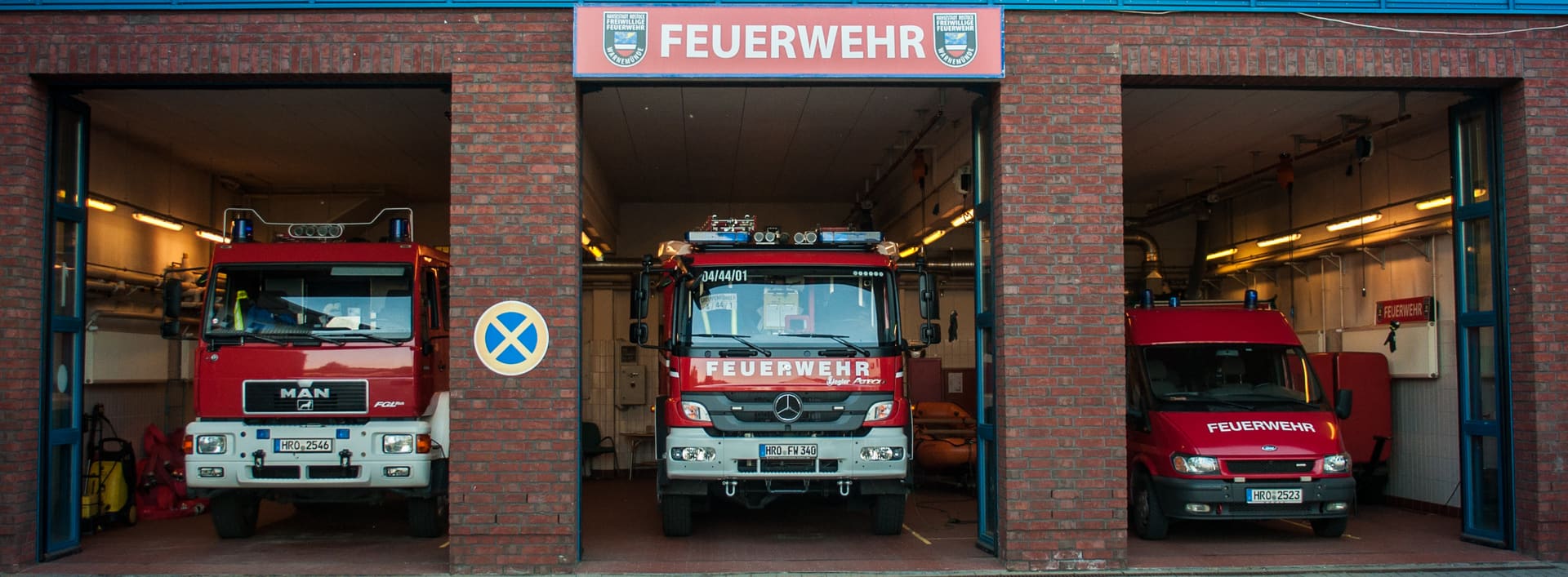 Das Gerätehaus der Freiwilligen Feuerwehr Warnemünde mit drei offenen Toren, davor ein Tanklöschfahrzeug, ein Löschfahrzeug und ein Mannschaftstransportwagen